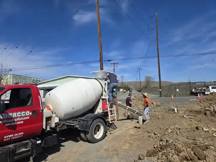 Red Soracco mixer pouring at a hillside job site, crew working the chute