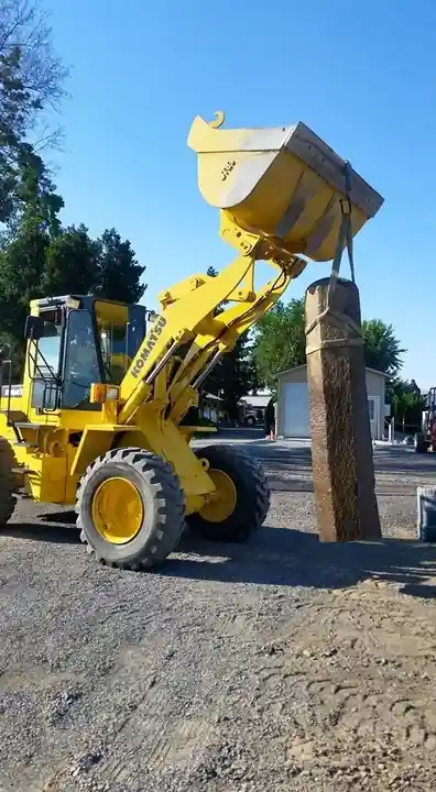 Yellow wheel loader holding a basalt column upright in the yard