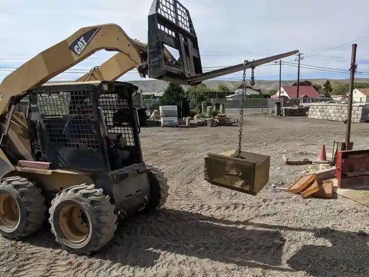 Skid steer lifting a World Block by chain in the Soracco yard
